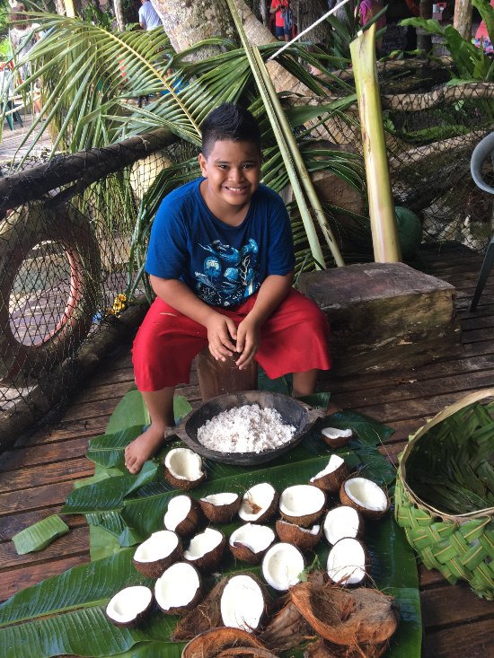 Young Samoan boy preparing coconut on banana leaves